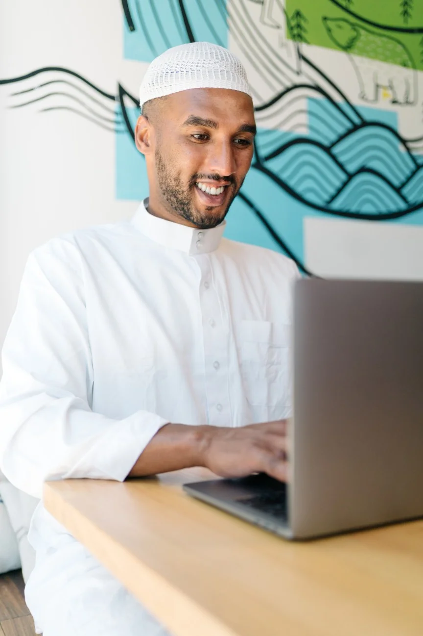 Muslim man smiling while using a laptop at a desk