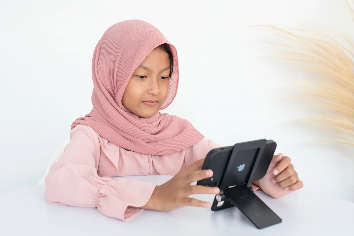 Girl in a pink hijab following an online Hifz lesson on a tablet
