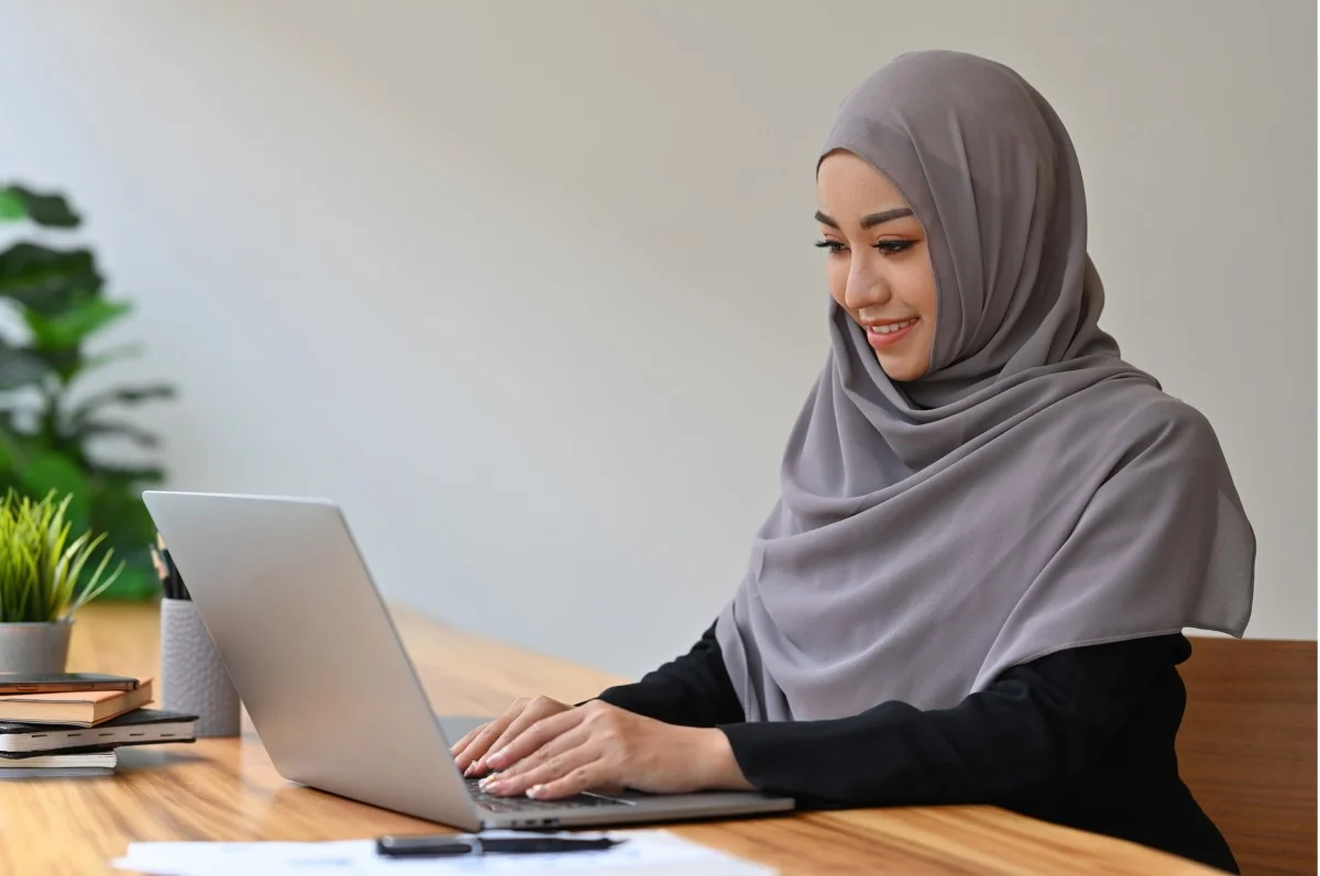 Muslim woman using a laptop at a home study desk