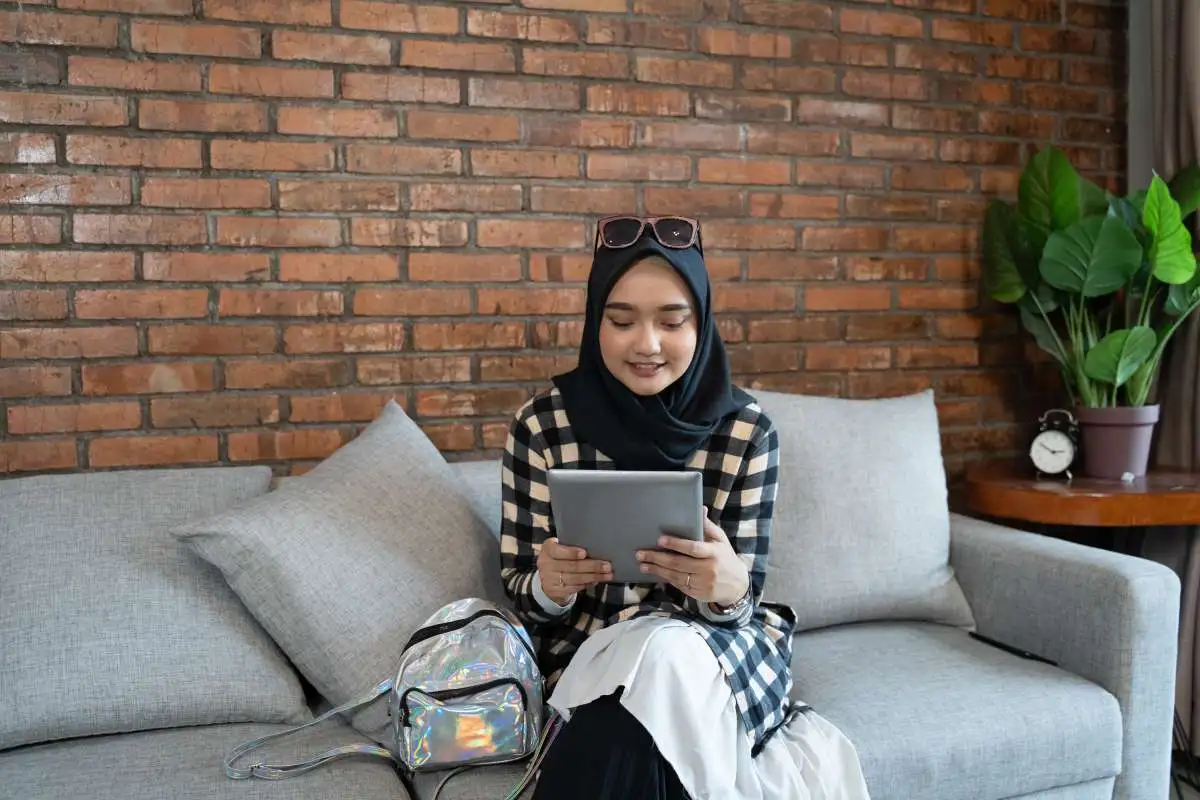 Muslim woman in a black hijab studying online with a tablet at home