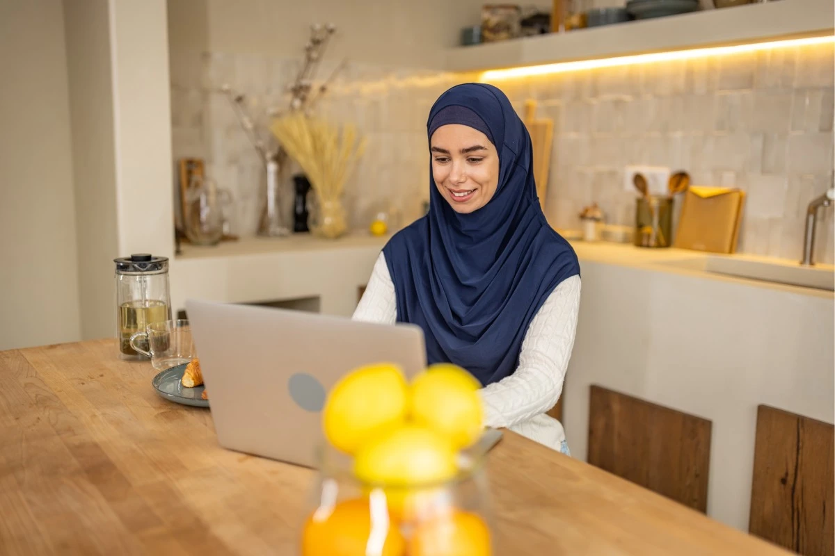 Muslim woman in a navy hijab studying online on a laptop at home