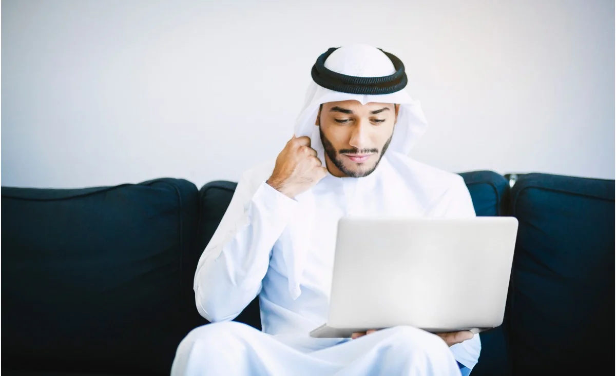 Muslim man using a laptop while seated on a sofa