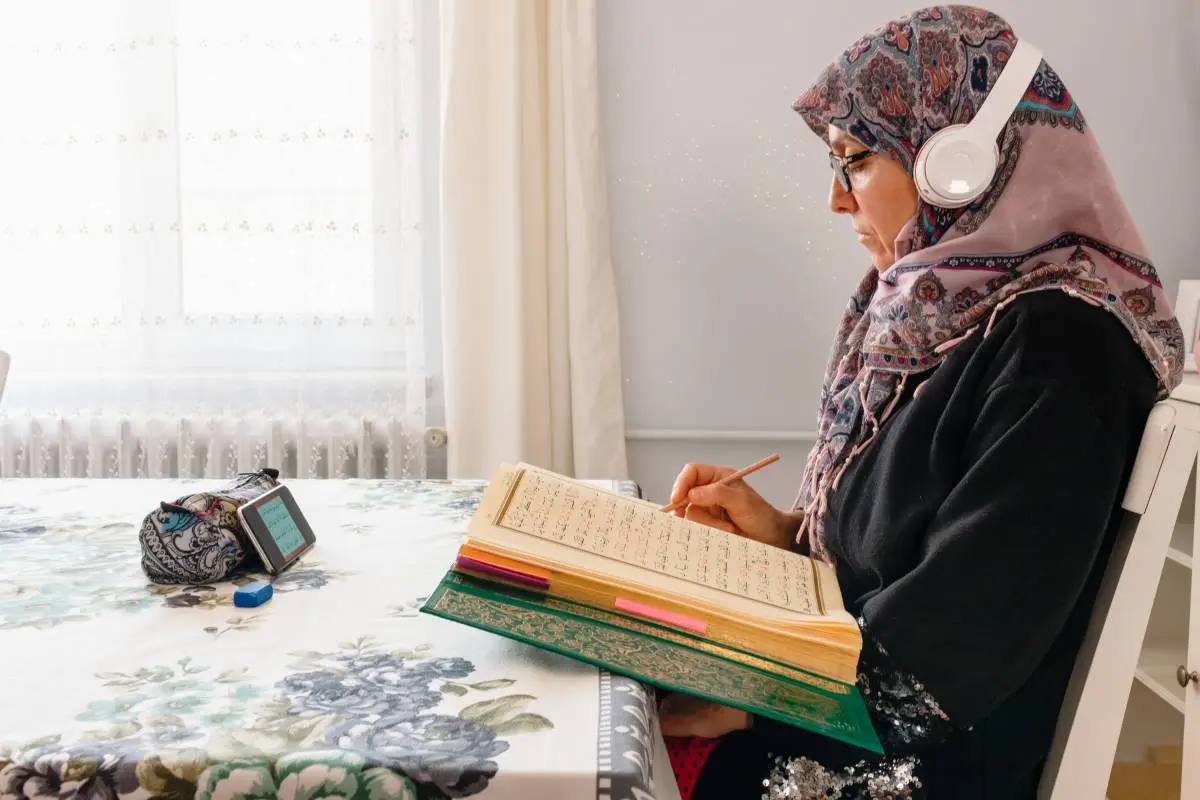 Adult Muslim woman wearing headphones and taking notes during an online Quran lesson