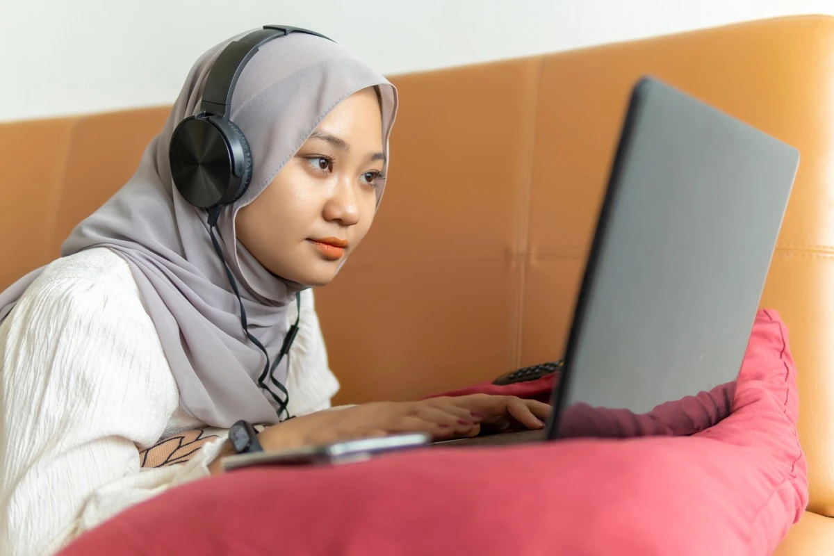 Muslim woman wearing headphones while studying through an online class on a laptop
