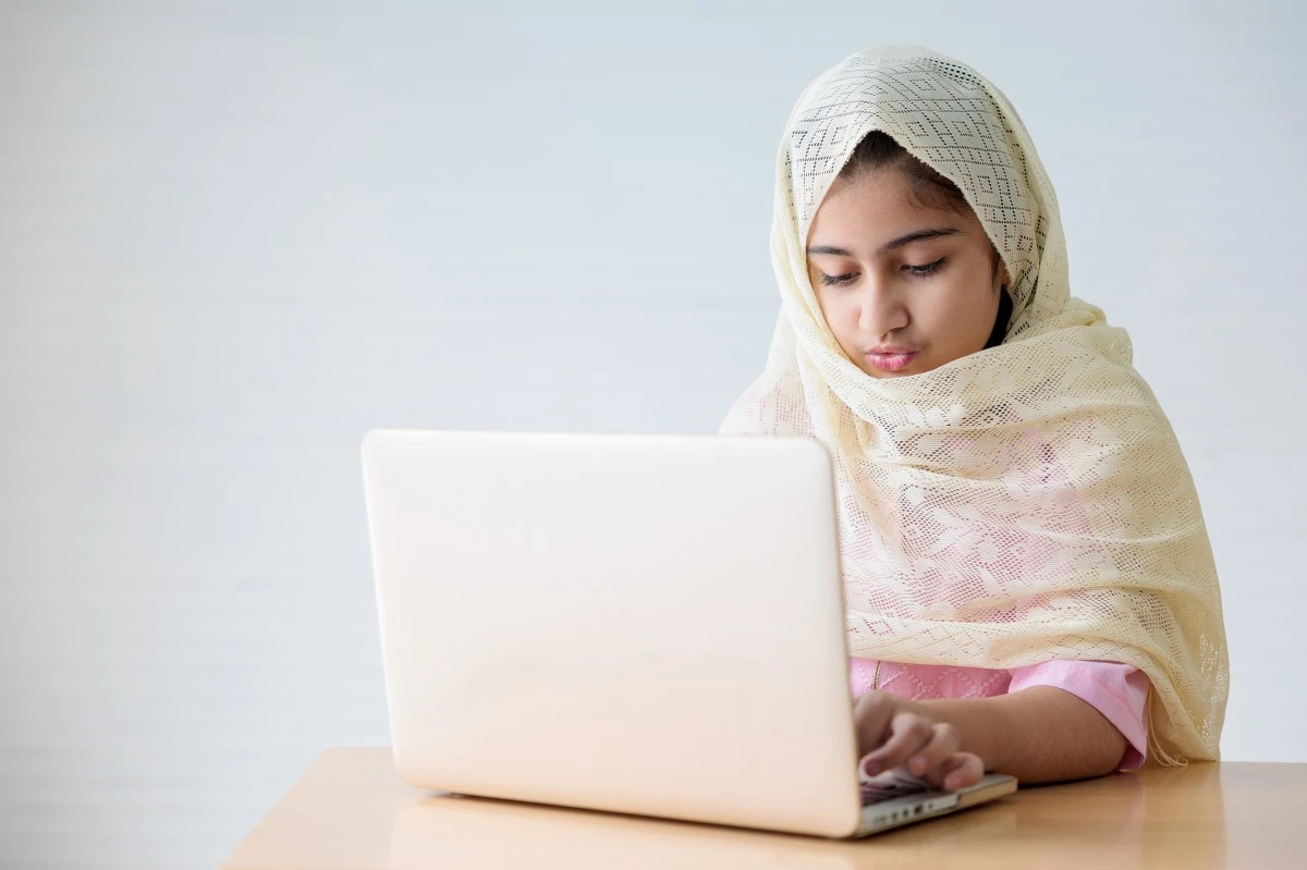 Young Muslim girl attending an online Quran class on a laptop at home