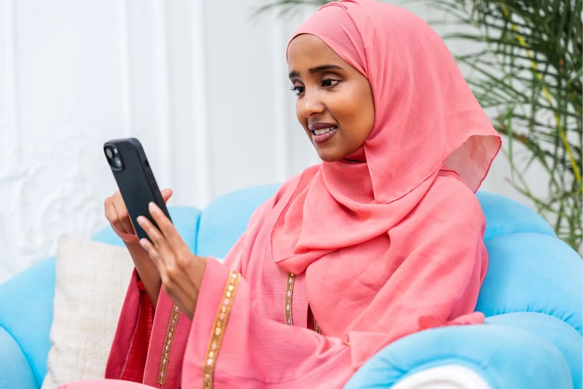 Muslim woman in a coral hijab joining an online lesson on her phone