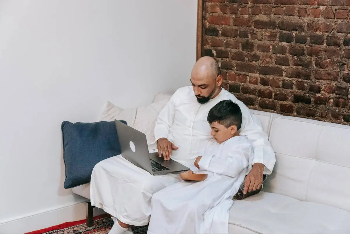 Father supporting his son during an online Quran lesson at home